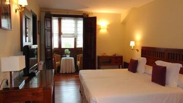 A hotel room with a bed, bedside table, lamp, desk, and a small table with a plant.