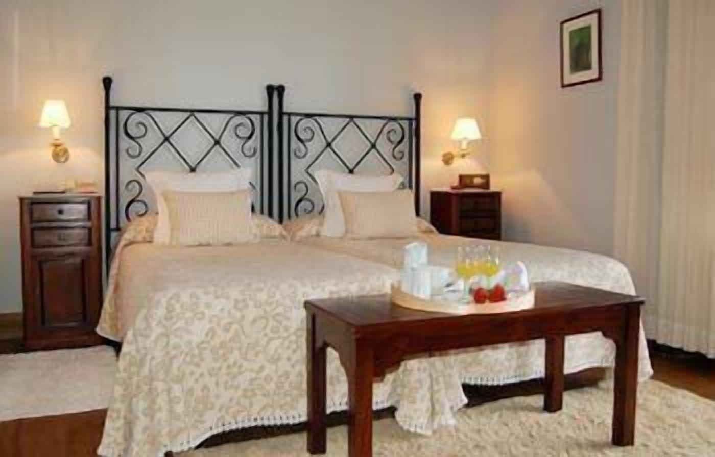 A neatly made bed with a patterned bedspread, two bedside tables with lamps, and a tray with breakfast items on the floor.