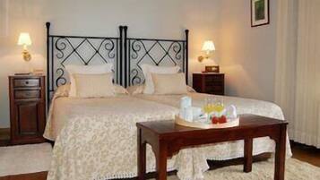 A neatly made bed with a patterned bedspread, two bedside tables with lamps, and a tray with breakfast items on the floor.