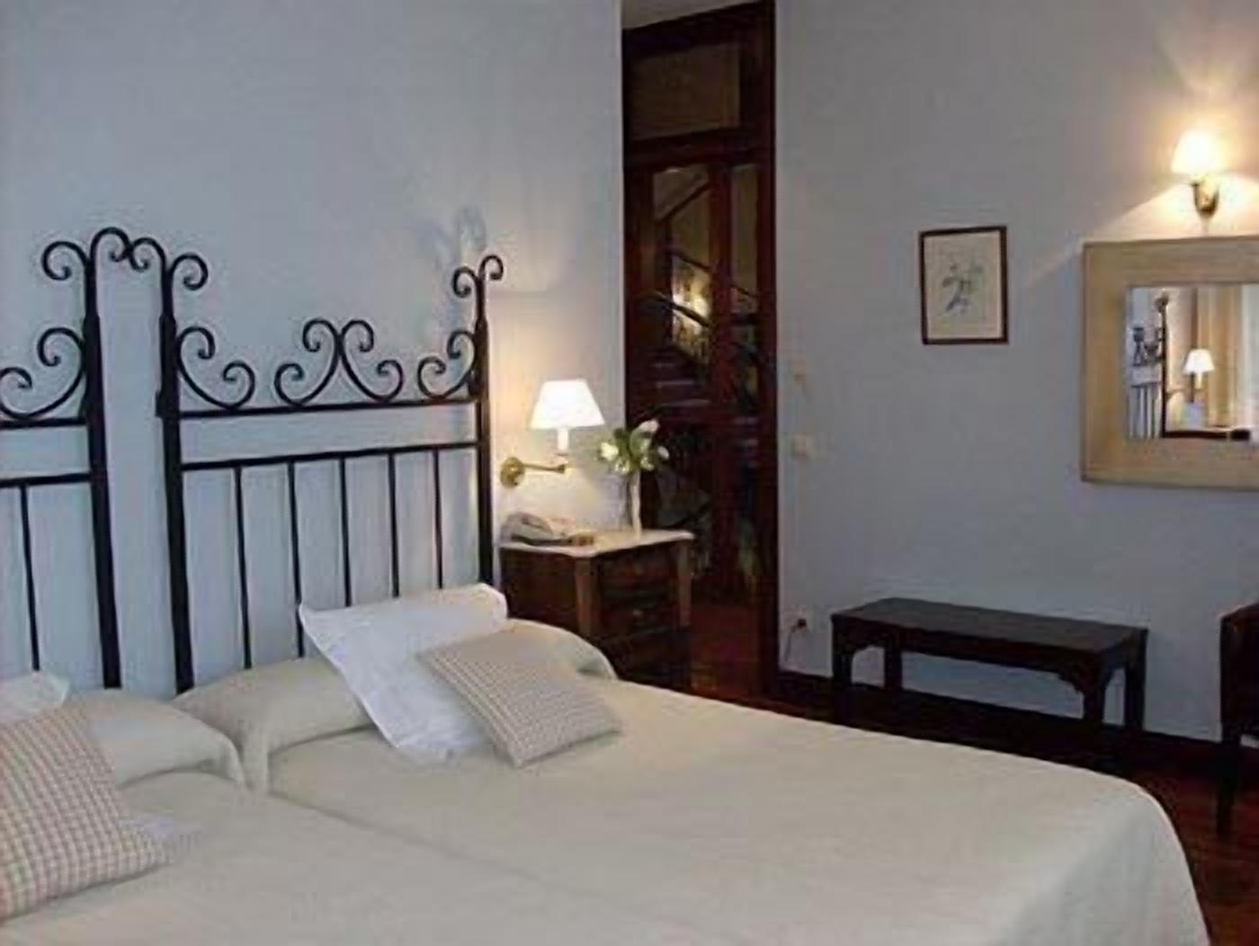 Un dormitorio con cama, mesita de noche, lámpara y espejo en la pared.