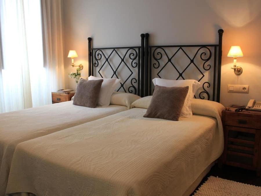 Una cama doble con cabecera metálica, dos mesitas de noche con lámparas y un teléfono junto a la cama.