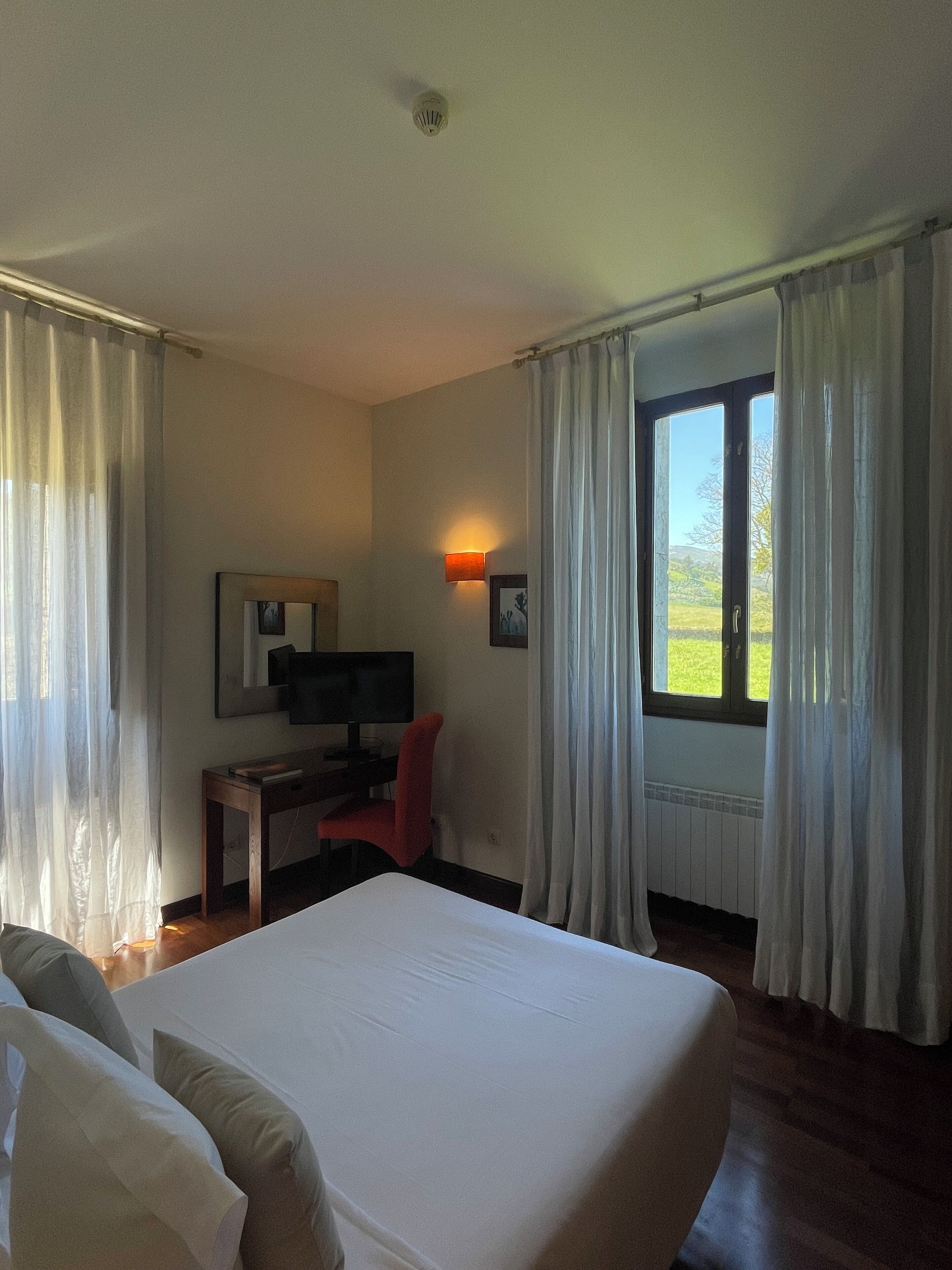 Habitación de hotel con cama, escritorio con silla, televisor y ventana con cortinas.