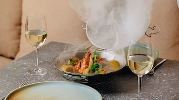 A dining table with a plate, a glass of white wine, and a steaming pot of food.