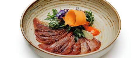 A ceramic bowl with a layered food presentation, including thinly sliced meat, greens, and a small orange element.