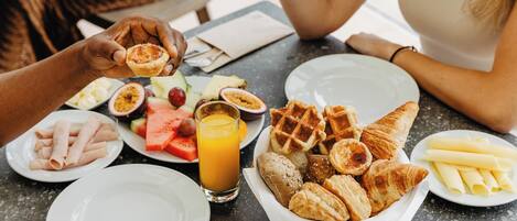 A breakfast table with various foods including waffles, croissants, and fruit.