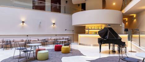 A modern lobby with a grand piano, seating areas, and a circular staircase.