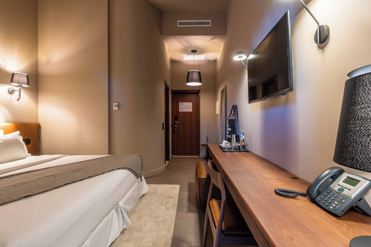 A hotel room with a bed, bedside table, lamp, phone, and a TV mounted on the wall.