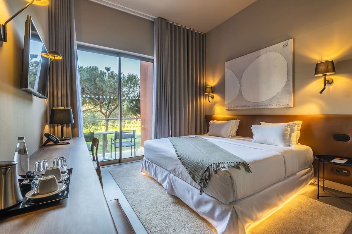 Une chambre d’hôtel avec un grand lit, un bureau doté d’un téléphone et d’un porte-lunettes, une machine à café et une vue sur l’extérieur.