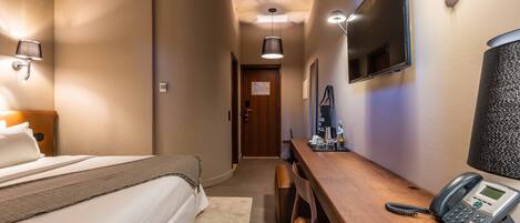 Habitación de hotel con cama, mesita de noche, lámpara, teléfono y televisor montado en la pared.