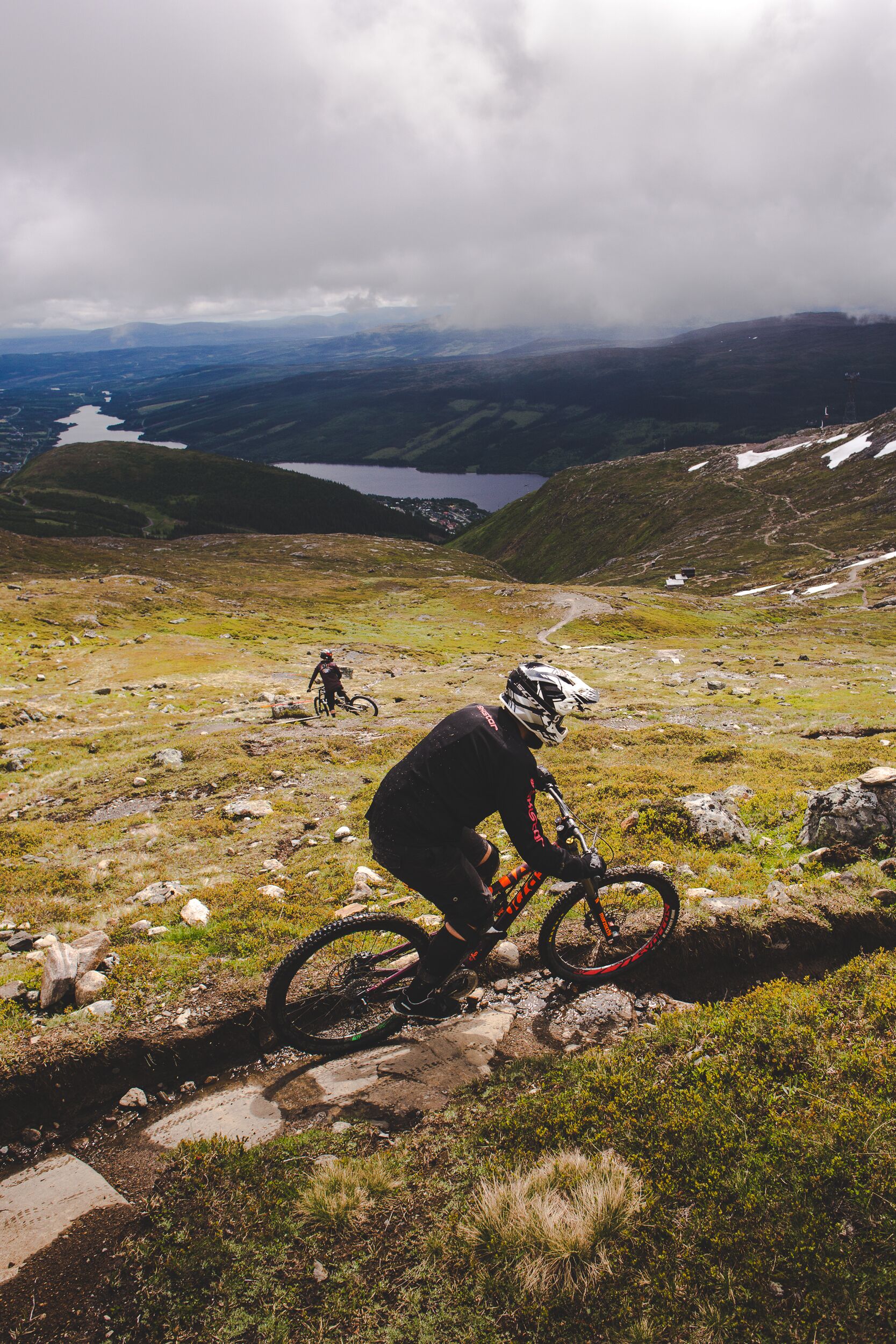 A mountain biker on a trail with a lake and mountains in the background.