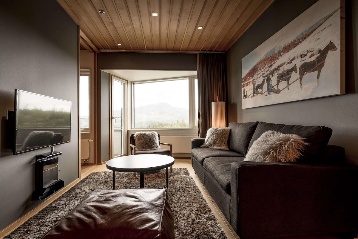 Ein modernes Wohnzimmer mit großem Fenster, Flachbildfernseher, Sofa und Couchtisch.