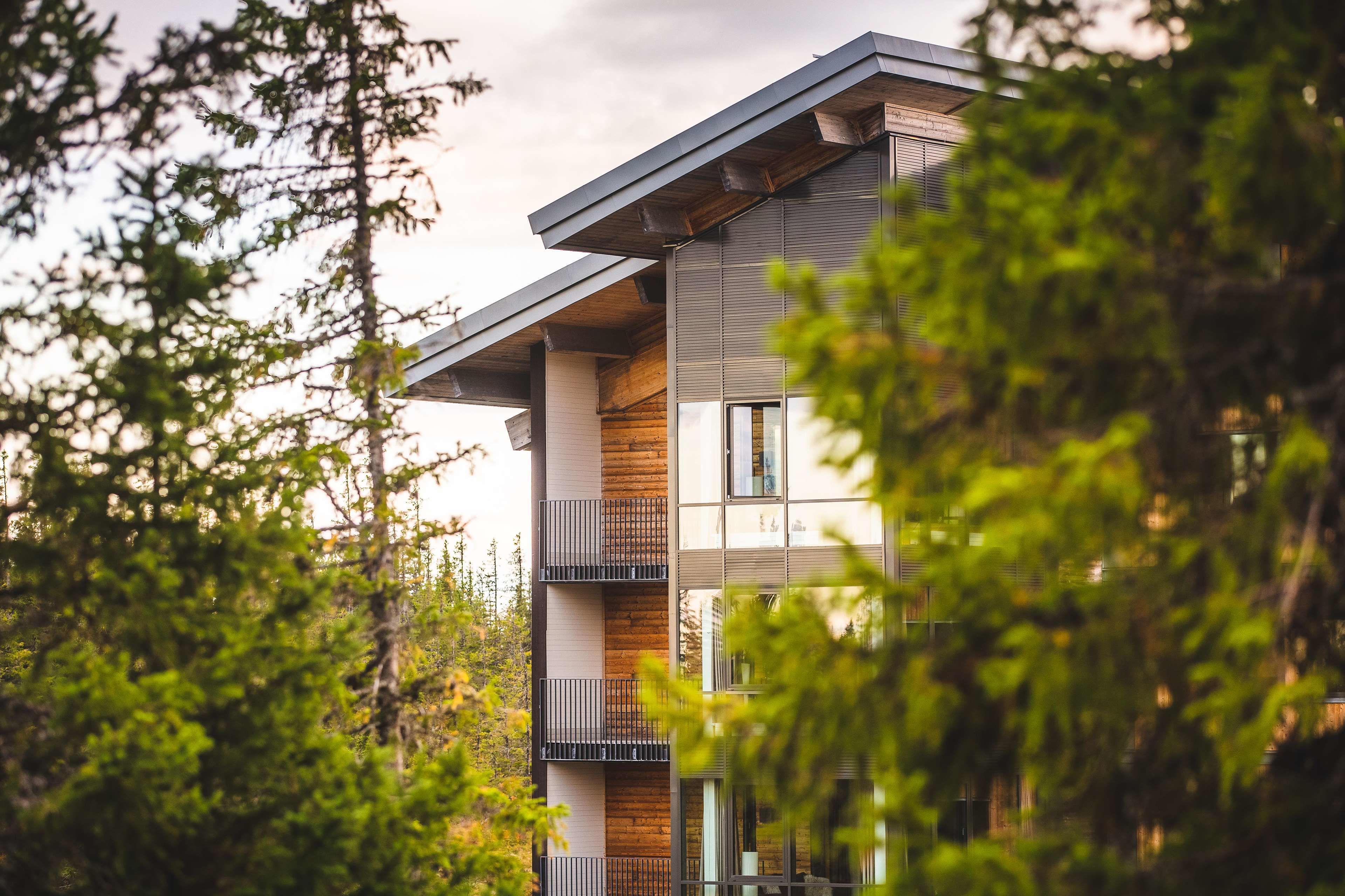 A modern multi-story building with balconies and large windows, surrounded by trees.