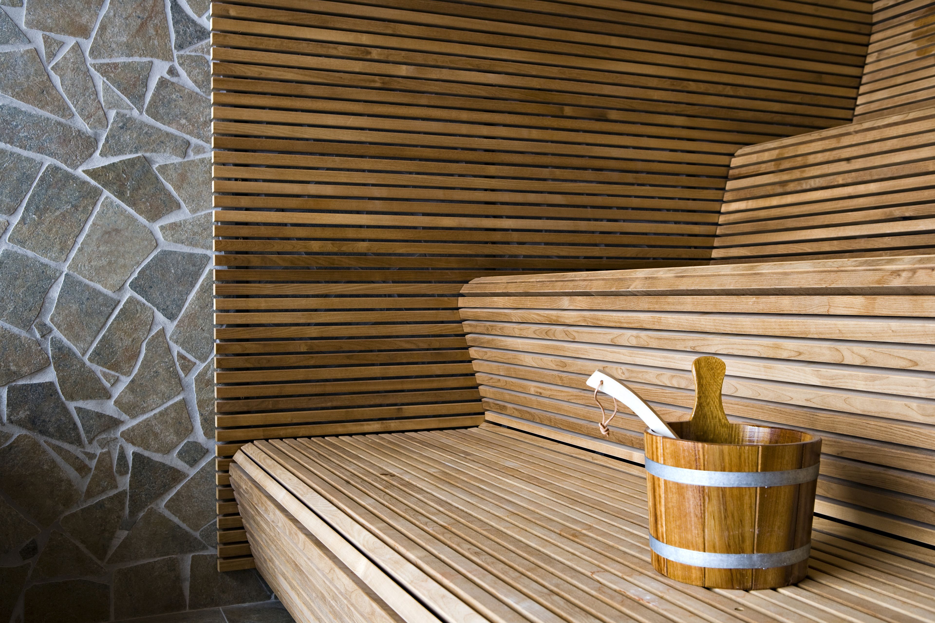 A wooden bench with a stone wall and a wooden bucket with a handle.