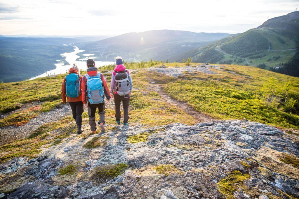 Tre vandrare på en stenig stig med en sjö och berg i bakgrunden.