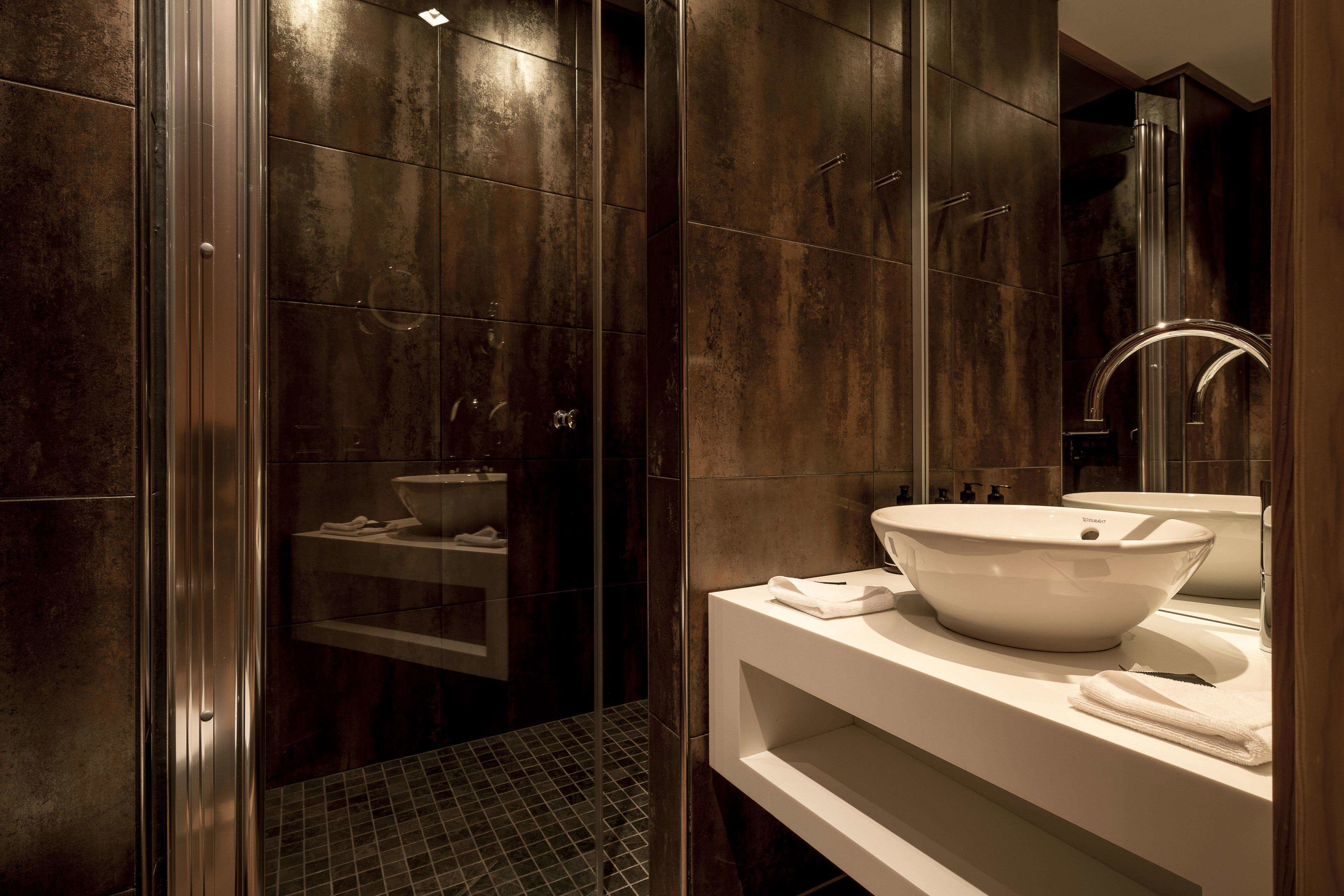 Un baño moderno con un espejo grande, un lavabo blanco y una zona de ducha con mampara de cristal.