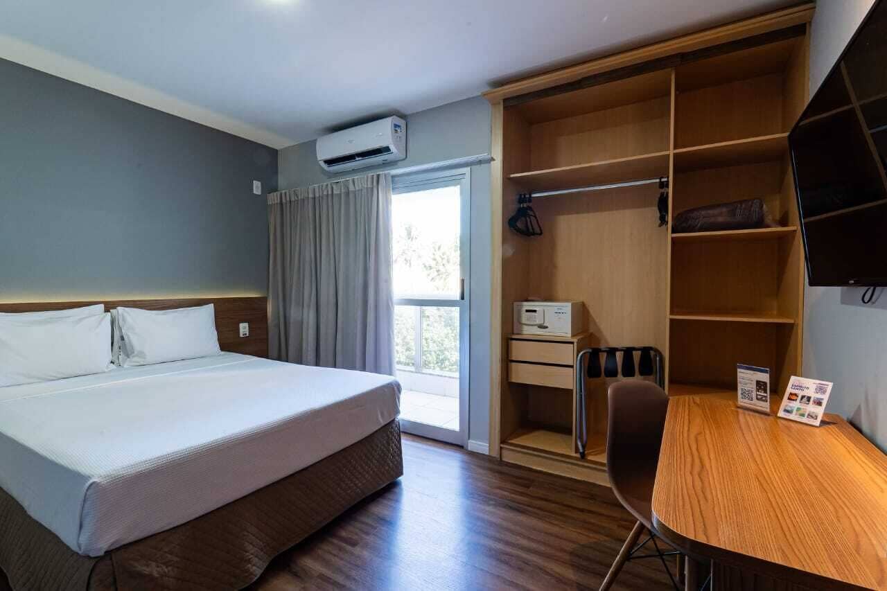 Habitación de hotel con cama, escritorio, silla, armario y aire acondicionado.