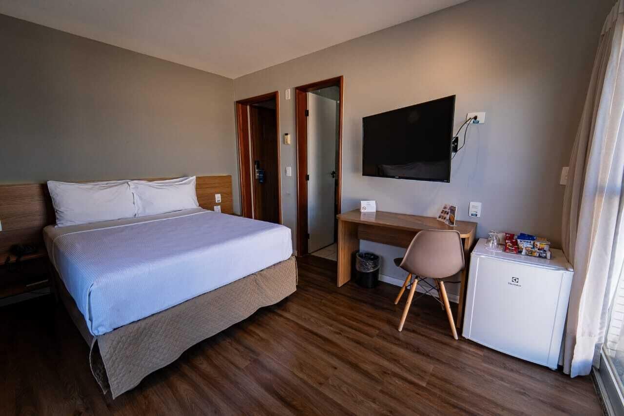 A hotel room with a bed, a desk, a television, and a refrigerator.