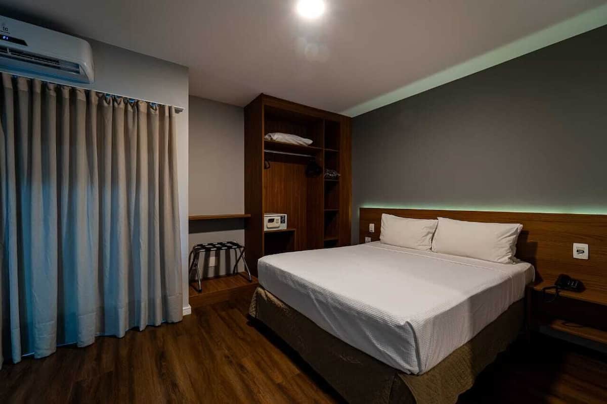 Habitación de hotel con cama, armario de madera y equipo de aire acondicionado.