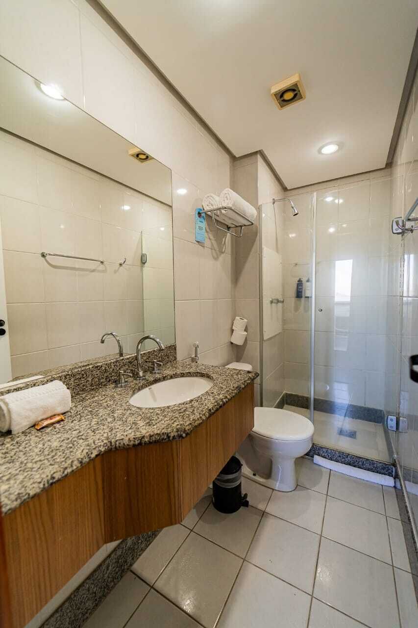 Een moderne badkamer met een granieten aanrechtblad, twee wastafels, een toilet en een douche met glazen wanden.