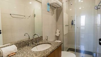 Een moderne badkamer met een granieten aanrechtblad, twee wastafels, een toilet en een douche met glazen wanden.