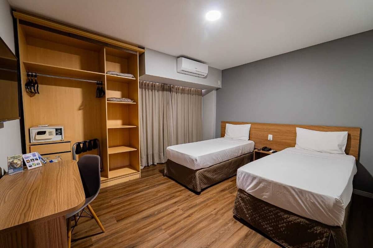 Habitación de hotel con dos camas, un armario de madera, un escritorio con silla y un microondas.
