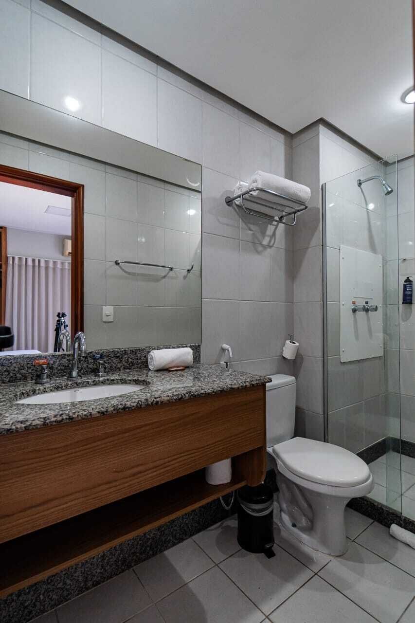 Un baño moderno con encimera de granito, inodoro blanco, cabina de ducha de vidrio y un espejo grande.