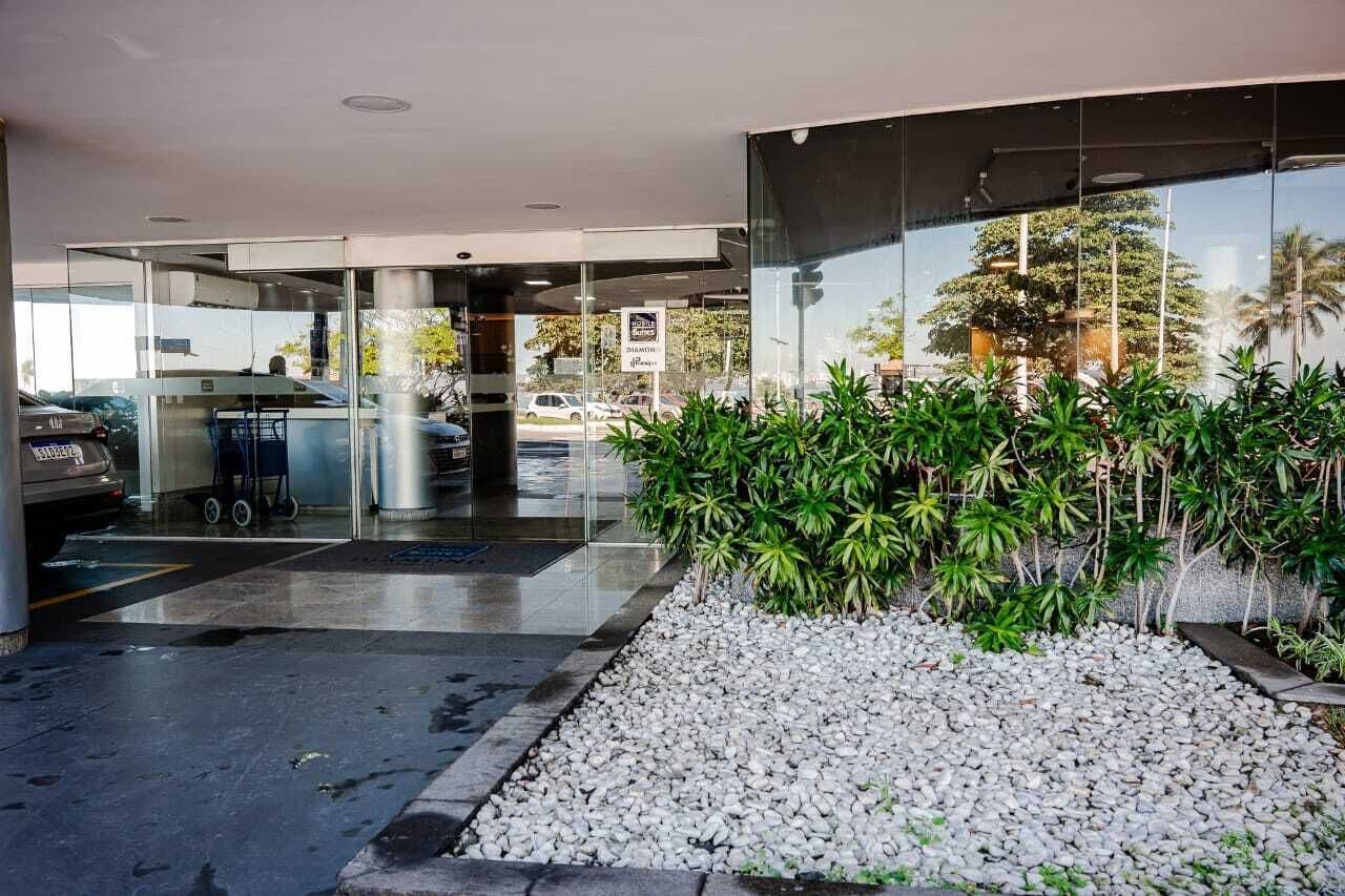 Een moderne gevel van een gebouw met glas, een grindpad met beplanting en een auto in de achtergrond.