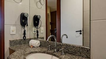 Un baño con lavamanos de encimera de granito, un espejo, dos secadores de pelo y una toalla.