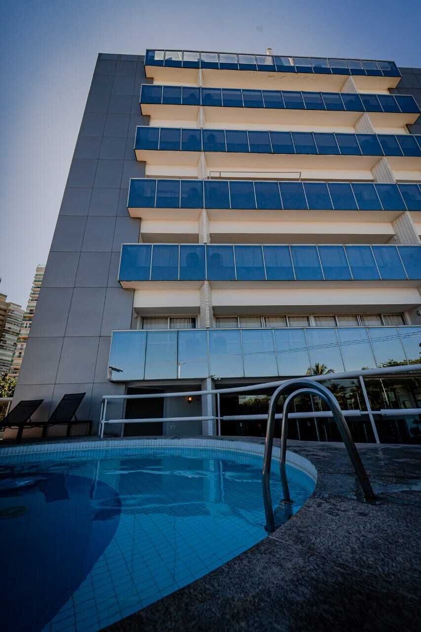 A modern hotel with a swimming pool, multiple balconies, and a clear view of the surrounding buildings.