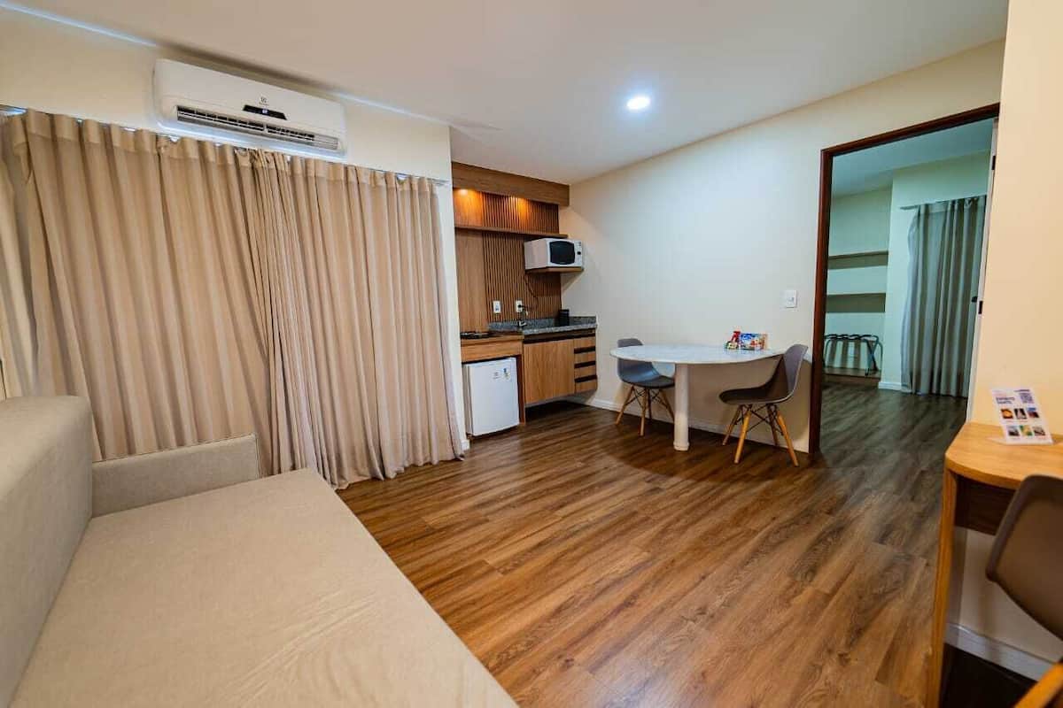 Una habitación compacta con cama, kitchenette, comedor y una puerta que da a otra habitación.