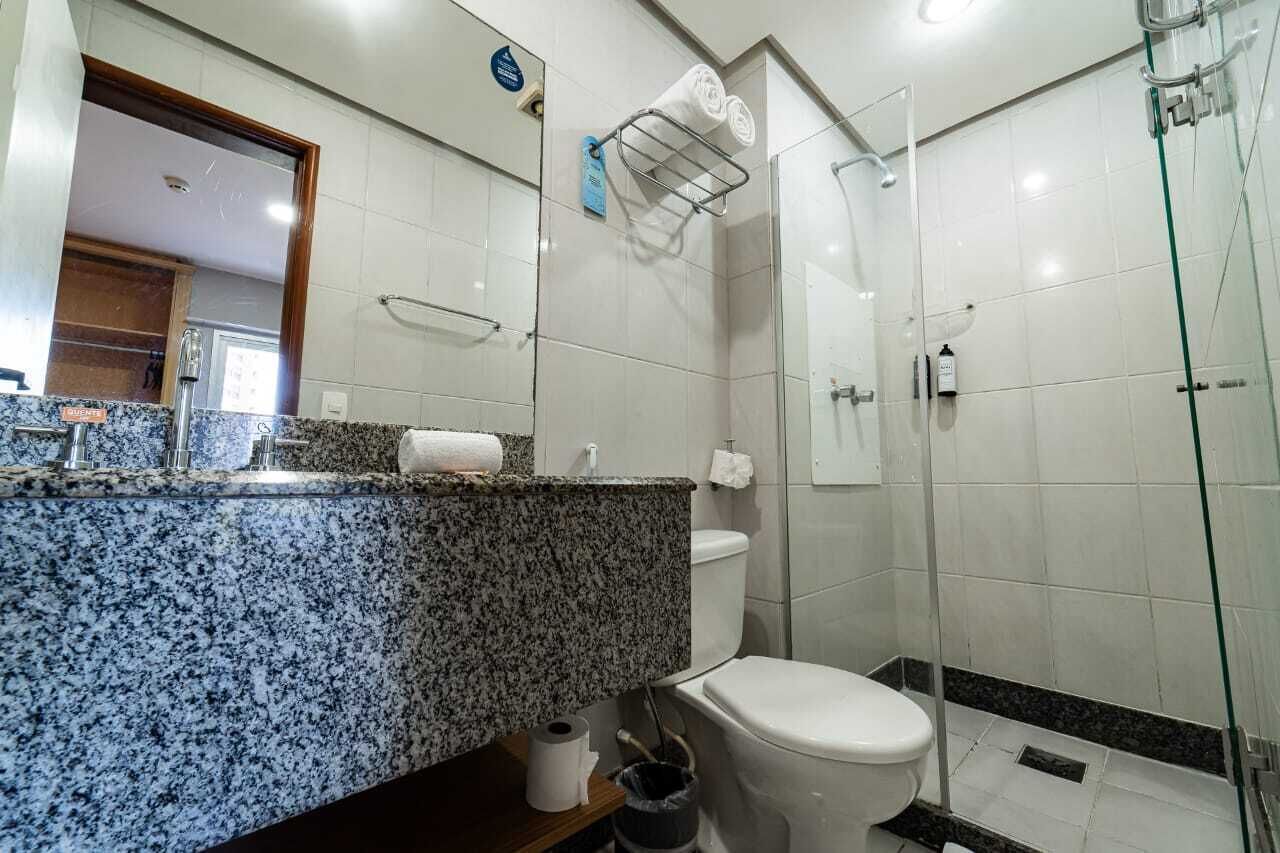 Un baño con encimera de granito, inodoro, cabina de ducha de vidrio y toallero.