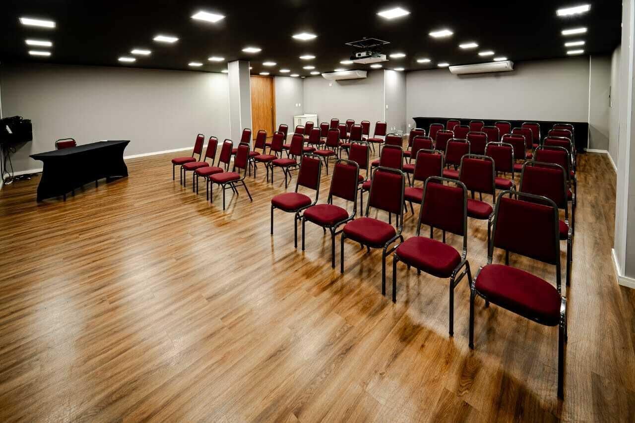 A conference room with rows of red chairs, a black table, and a wooden floor.
