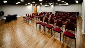 A conference room with rows of red chairs, a black table, and a wooden floor.