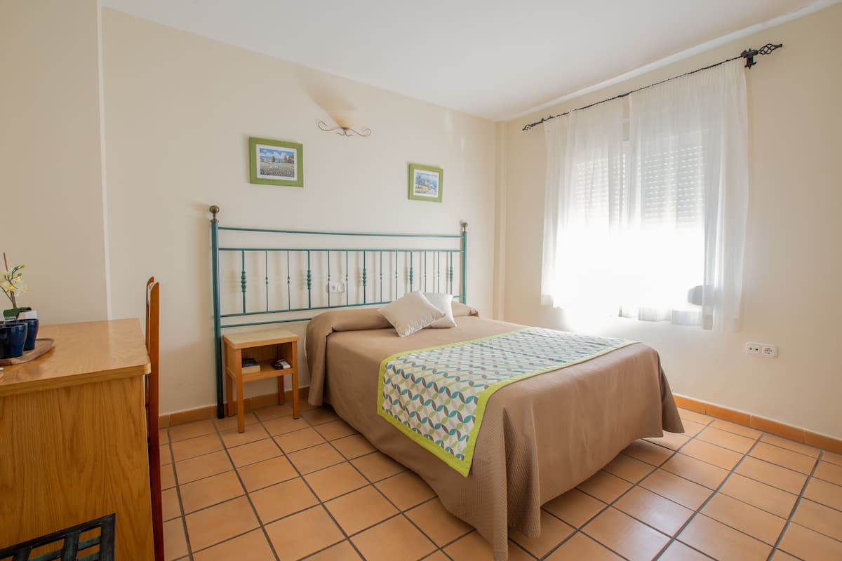 Ein Schlafzimmer mit einem Bett, einem Schreibtisch und einem Stuhl. An der Wand hängen zwei gerahmte Bilder.
