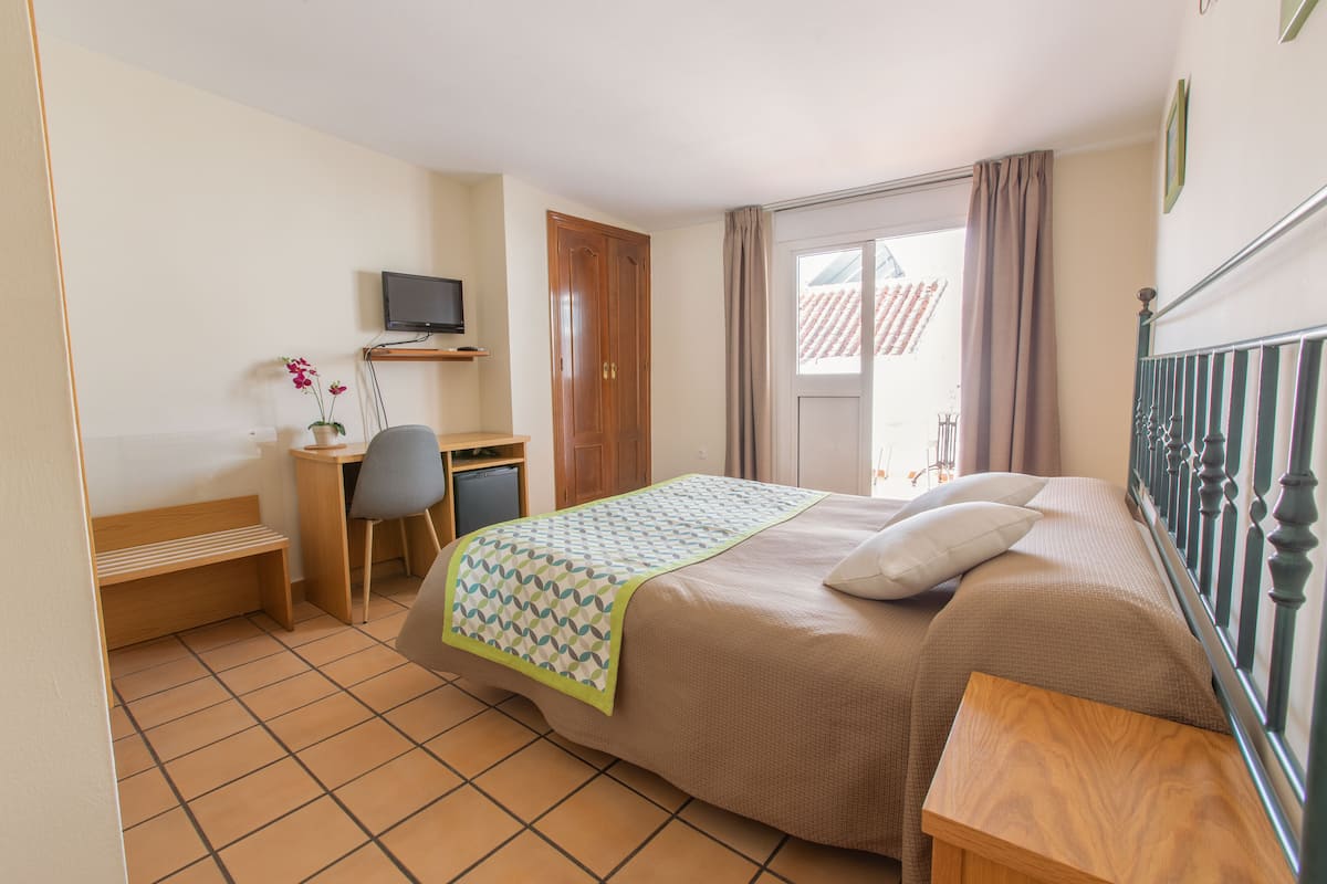 Ein Hotelzimmer mit einem Bett, einem Schreibtisch, einem Sessel, einem Fernseher und einem fenster mit Vorhängen.