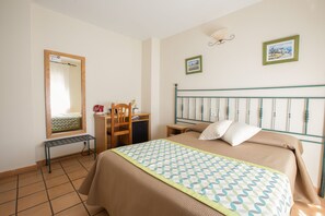 A bedroom with a bed, a desk, a chair, a small table, and a mirror. - Hostal El Gallo (Marbella)