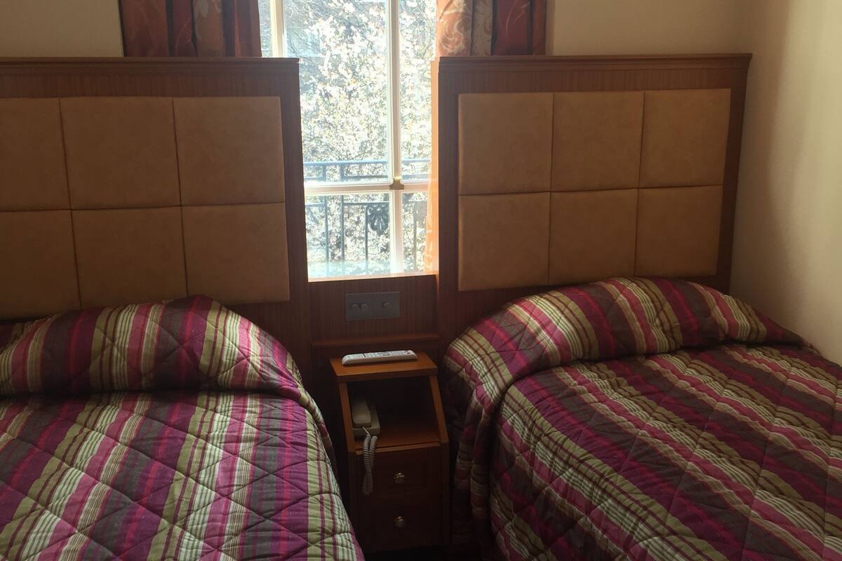 A room with two beds, a nightstand, and a window with curtains.