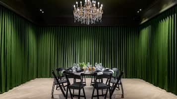 Un salón de conferencias con una mesa redonda dispuesta para seis personas, rodeada de sillas negras, una araña de cristal y paredes cubiertas con tela verde.