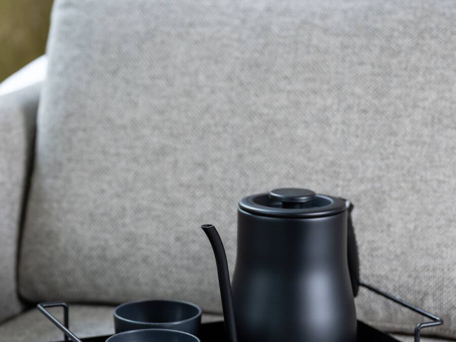 Una bandeja negra con una tetera y dos tazas sobre un sofá gris.