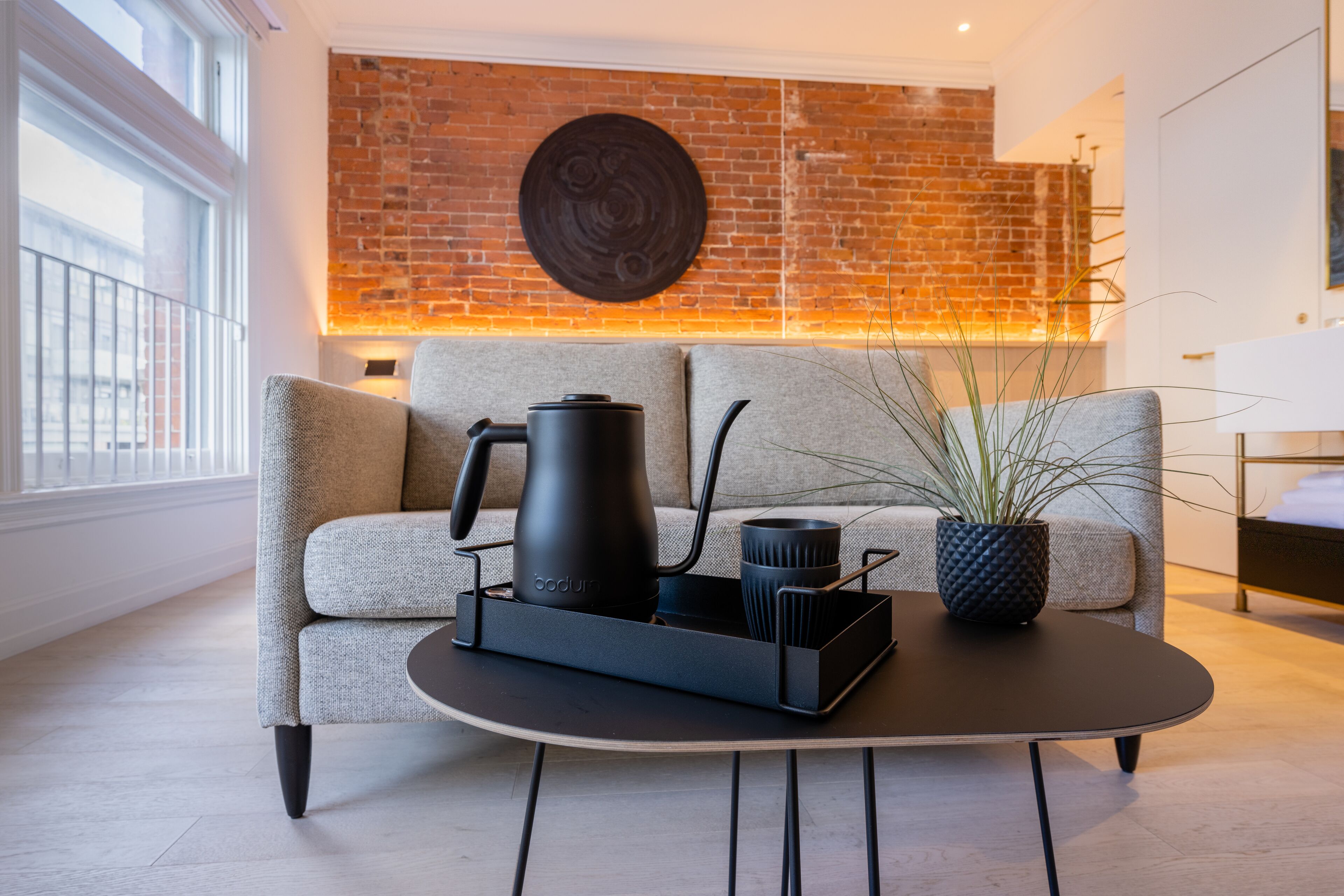 A modern living room with a sofa, a coffee table, a black kettle, and a potted plant.