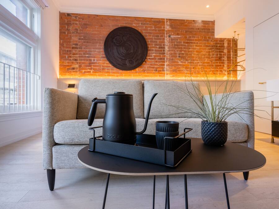 A modern living room with a sofa, a coffee table, a black kettle, and a potted plant.