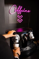 Een persoon bedient een koffieapparaat, erboven een neonbord met de tekst 'Caffeine'.