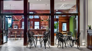 A spacious bar area with a brick wall backdrop, wooden furniture, and a view of the kitchen through large glass doors.