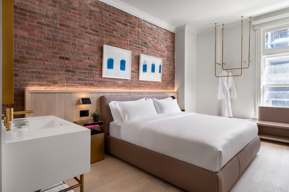 Une chambre à coucher moderne avec un mur en briques, un lit blanc, une table de chevet et un luminaire suspendu.