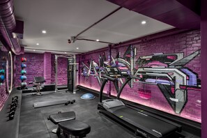 Un gimnasio con paredes moradas, equipo de ejercicios y un espejo grande.