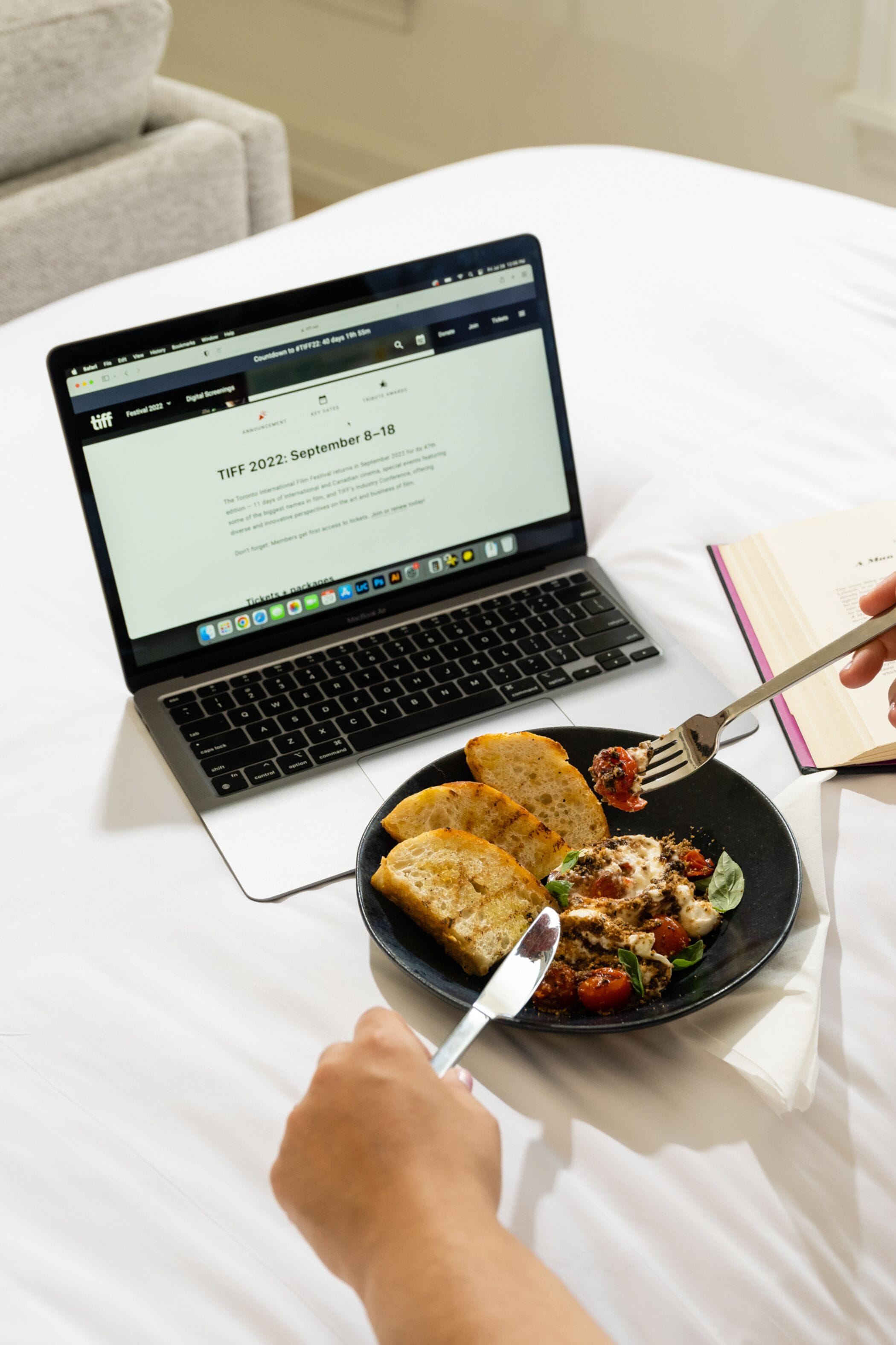 Una laptop sobre la cama con un plato de comida y un tenedor.