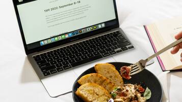 Una laptop sobre la cama con un plato de comida y un tenedor.
