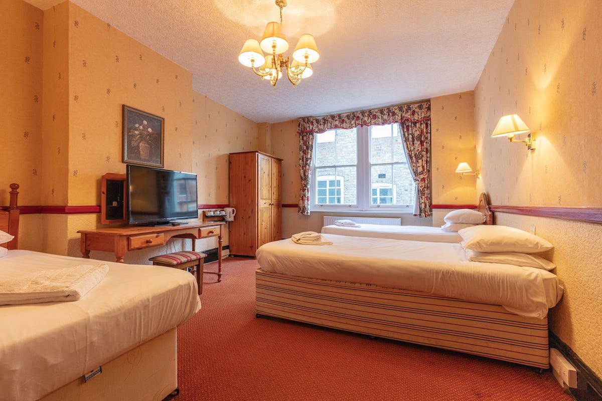 A hotel room with two beds, a television, a desk, and a window with curtains.
