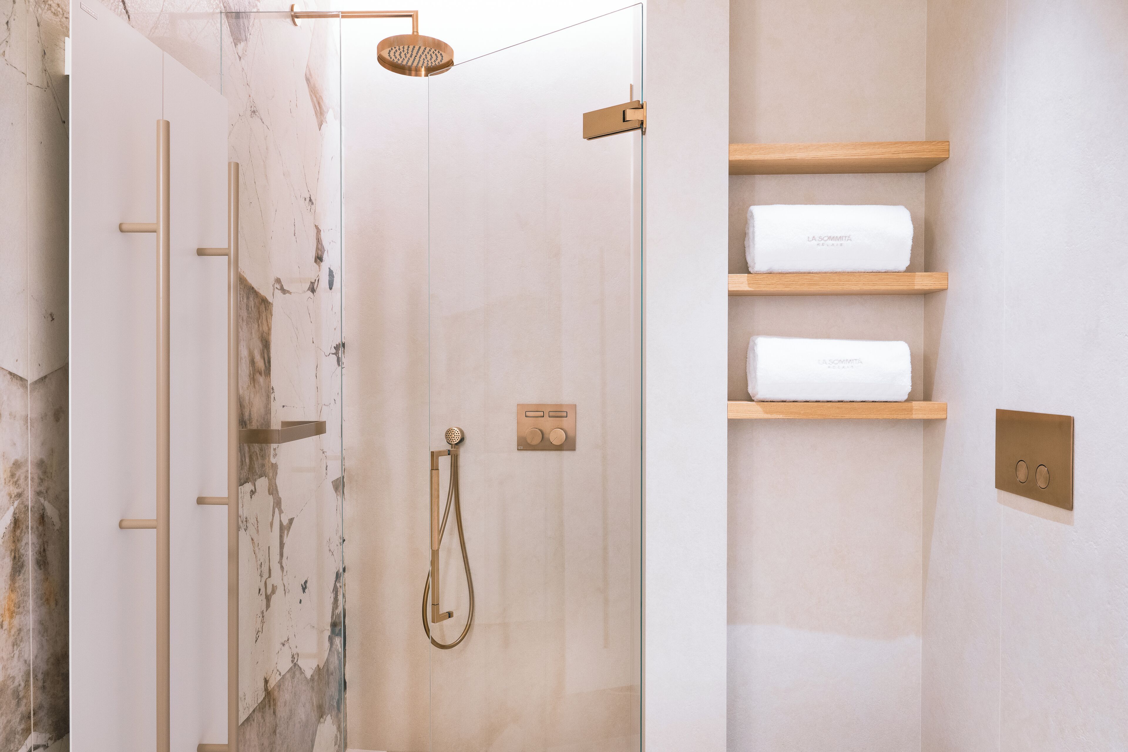 Ein modernes Badezimmer mit einer gläsernen Duschkabine, Marmorwänden und Holzböden mit Handtüchern.