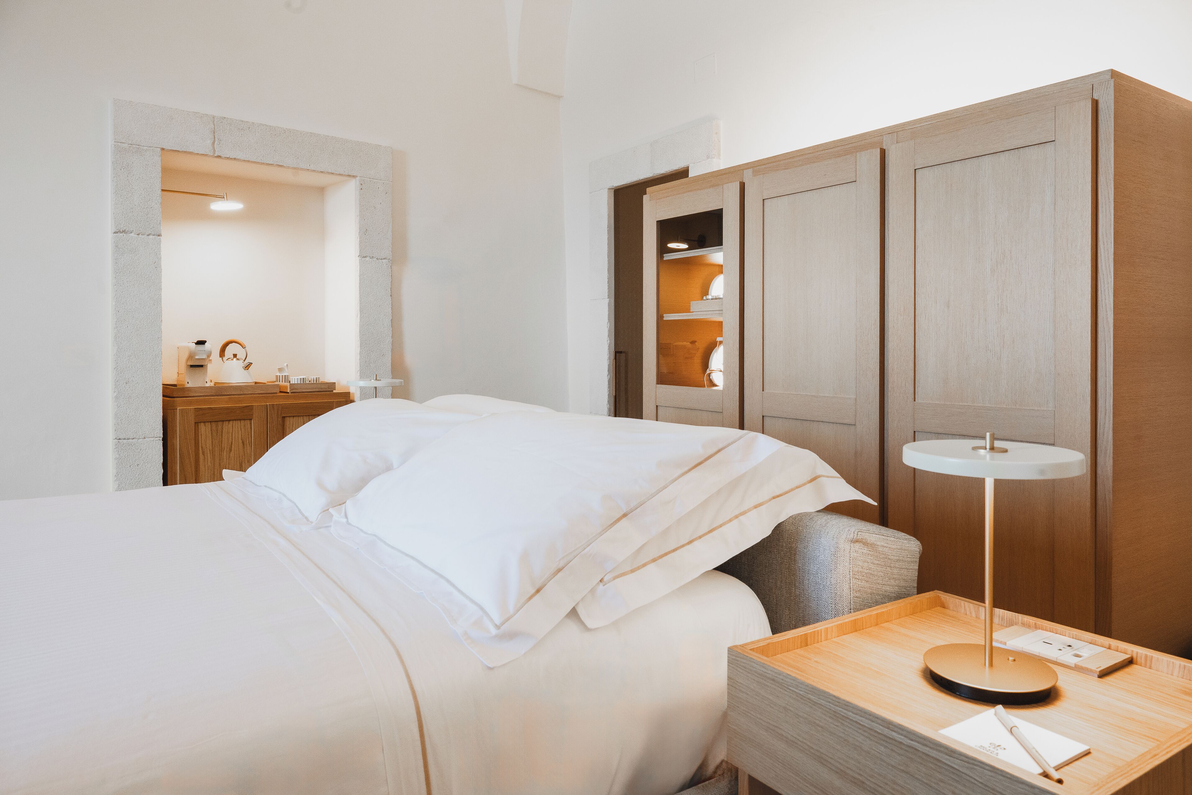 A hotel room with a bed, bedside table, lamp, and a wooden wardrobe.
